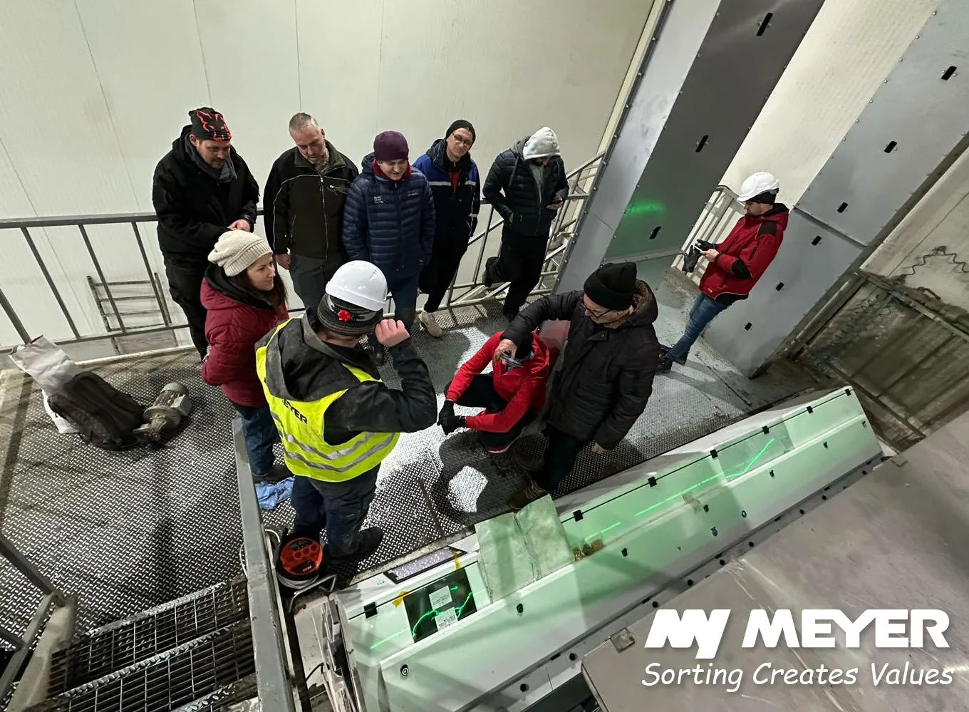 Customers and MEYER specialists during an on-site demonstration of an optical sorting installation in an industrial processing facility.